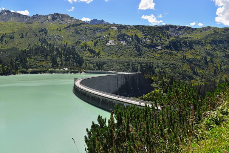 a lake and dam in front of a backdrop of green mountains